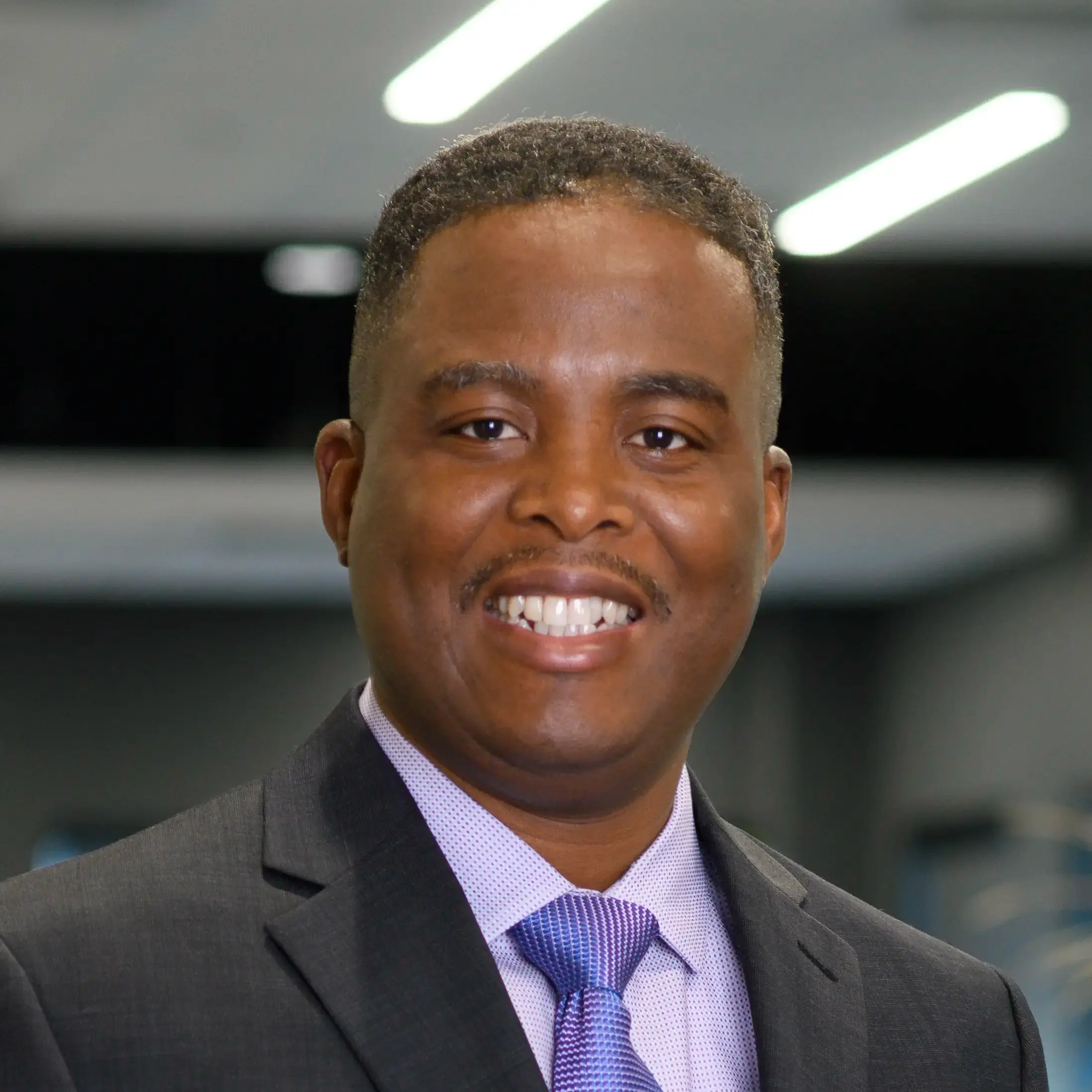 Dami Adedapo smiles warmly while standing in an office setting.