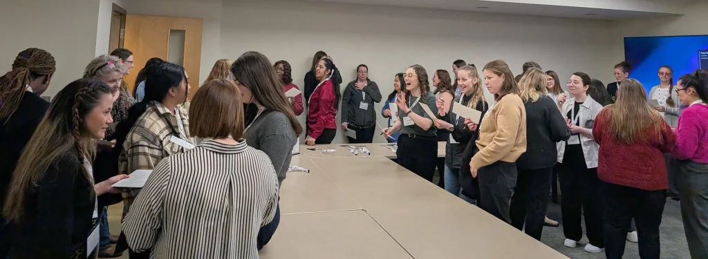 A large group of KGS women employees gather together and engage in conversation in an office setting.