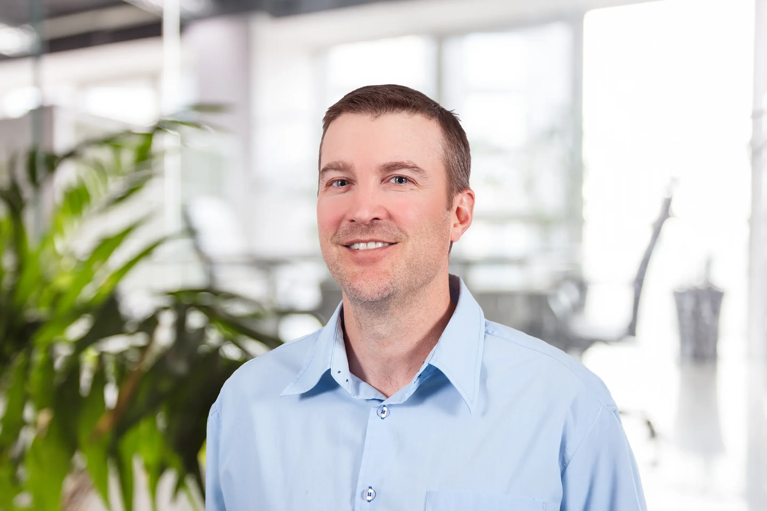 Brent Tombs smiles warmly while posing in a plant-filled office.