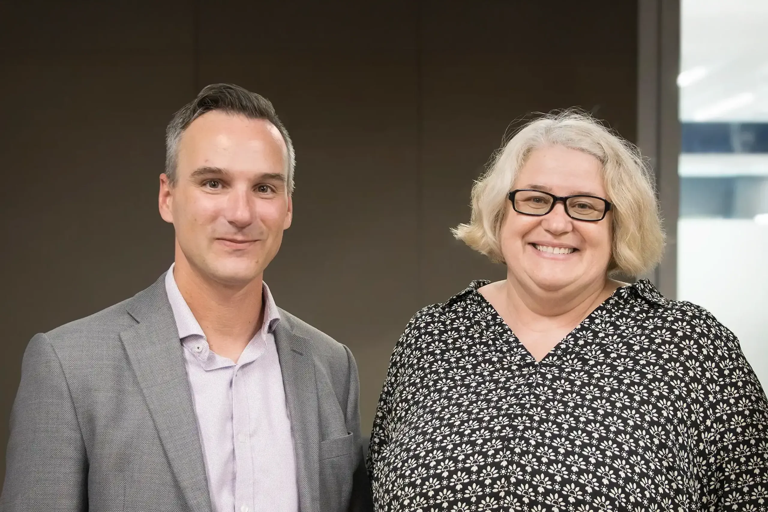 Two KGS employees, each celebrating 25 years with the company, smile warmly as they stand together in an office setting.