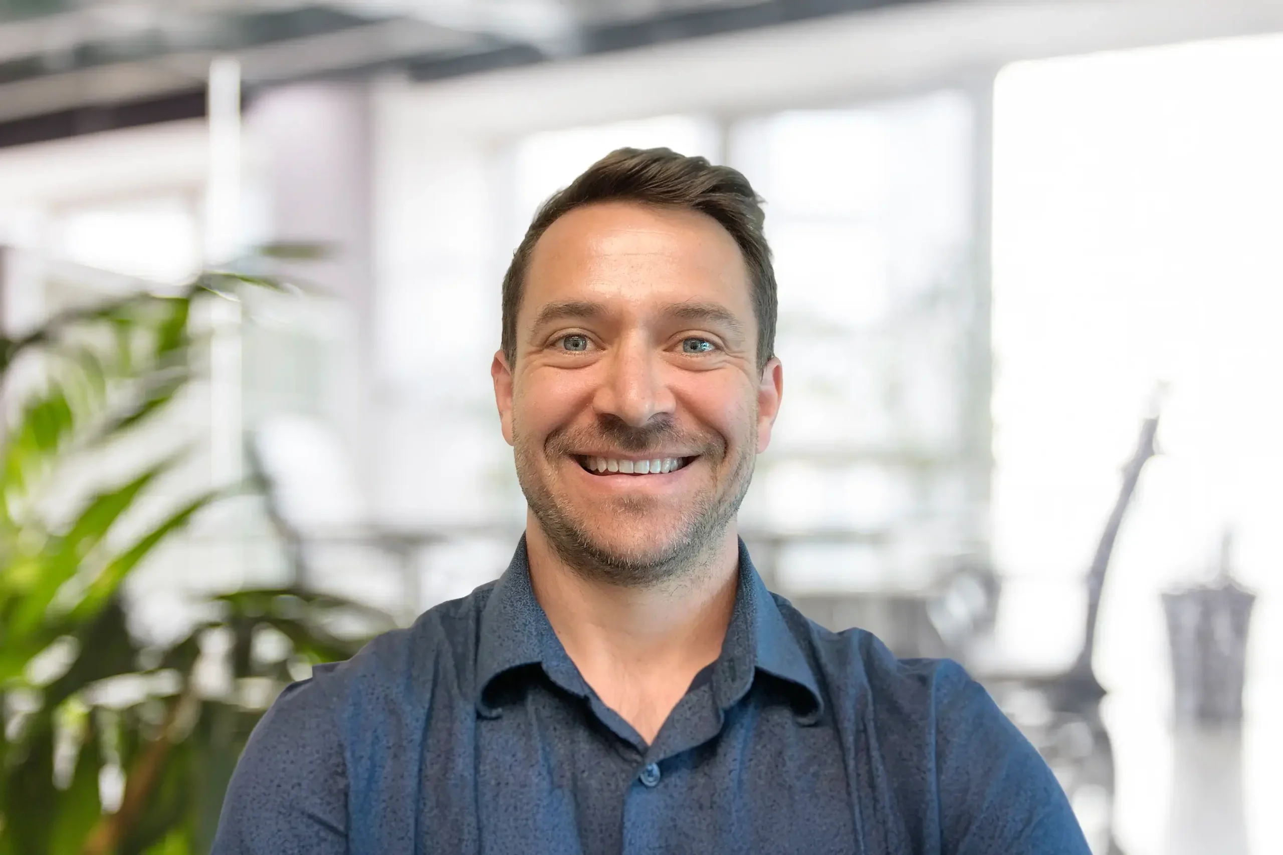 Dan Sims smiles warmly while sitting in a plant-filled office setting.