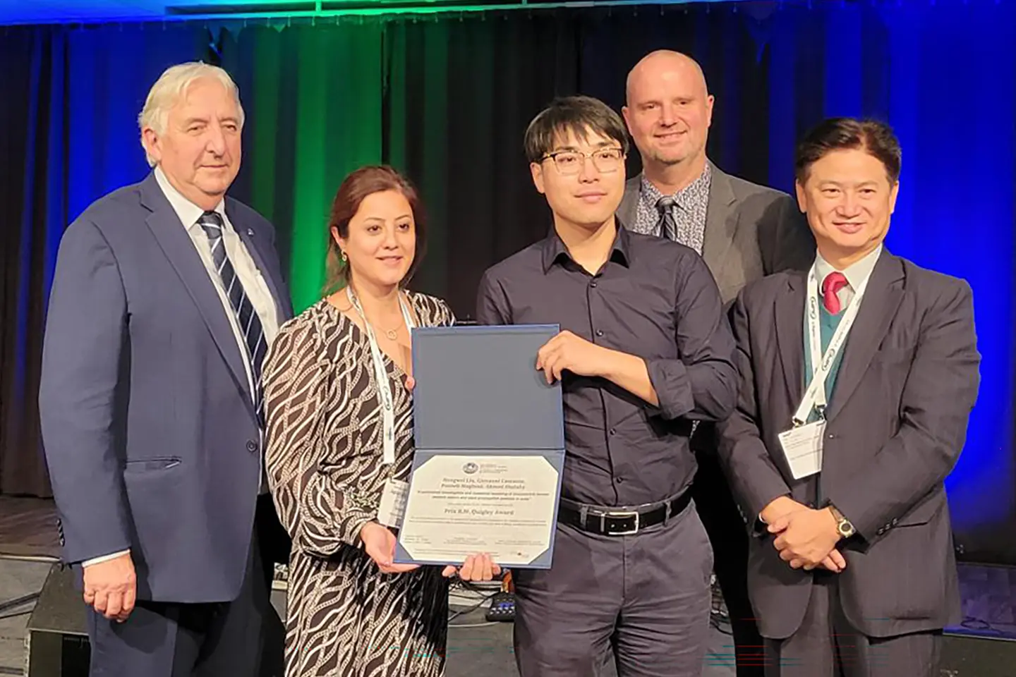 Dr. Hongwei Liu receives an award while surrounded by colleagues.