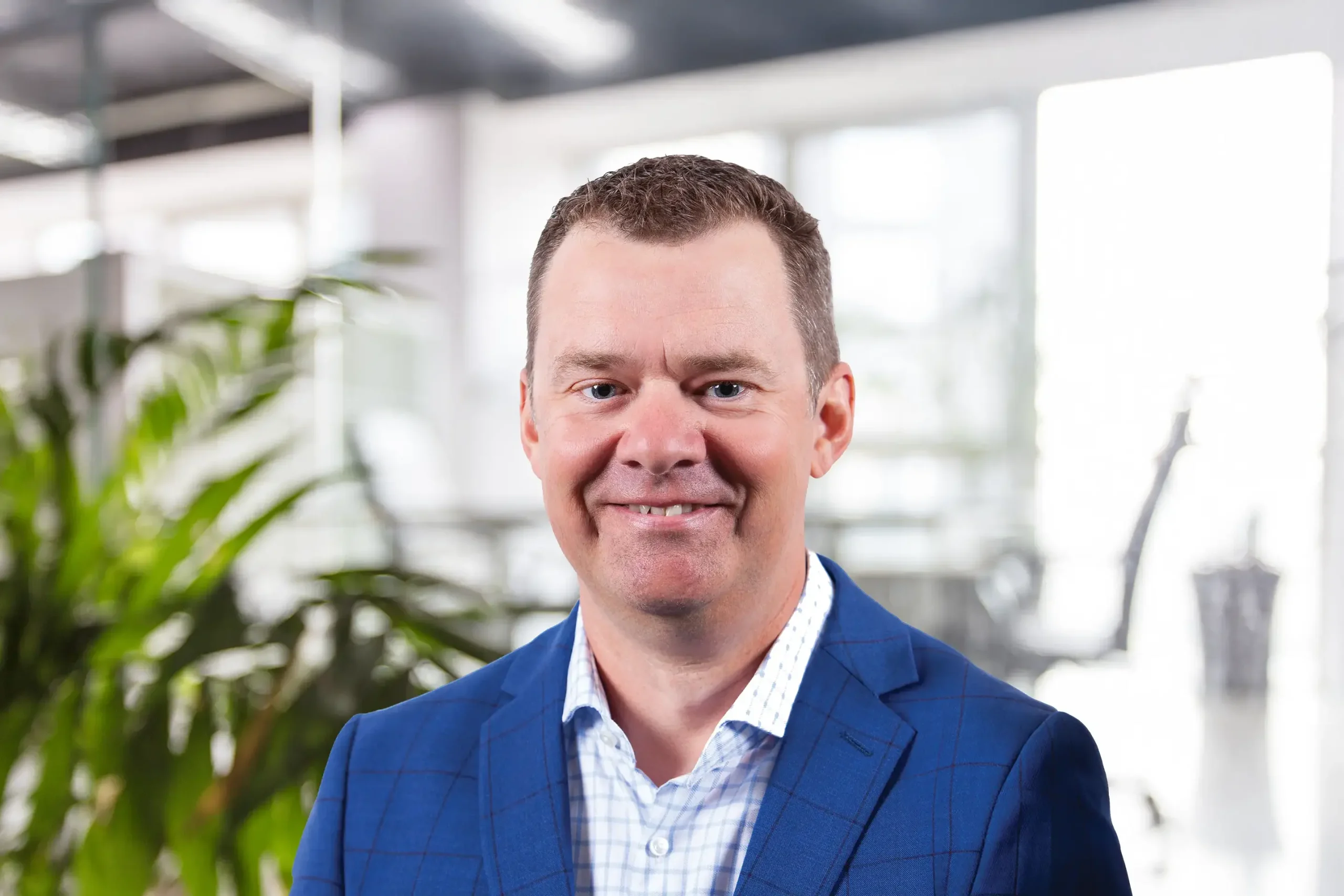 Jon Friesen smiles warmly while standing in a plant-filled office setting.