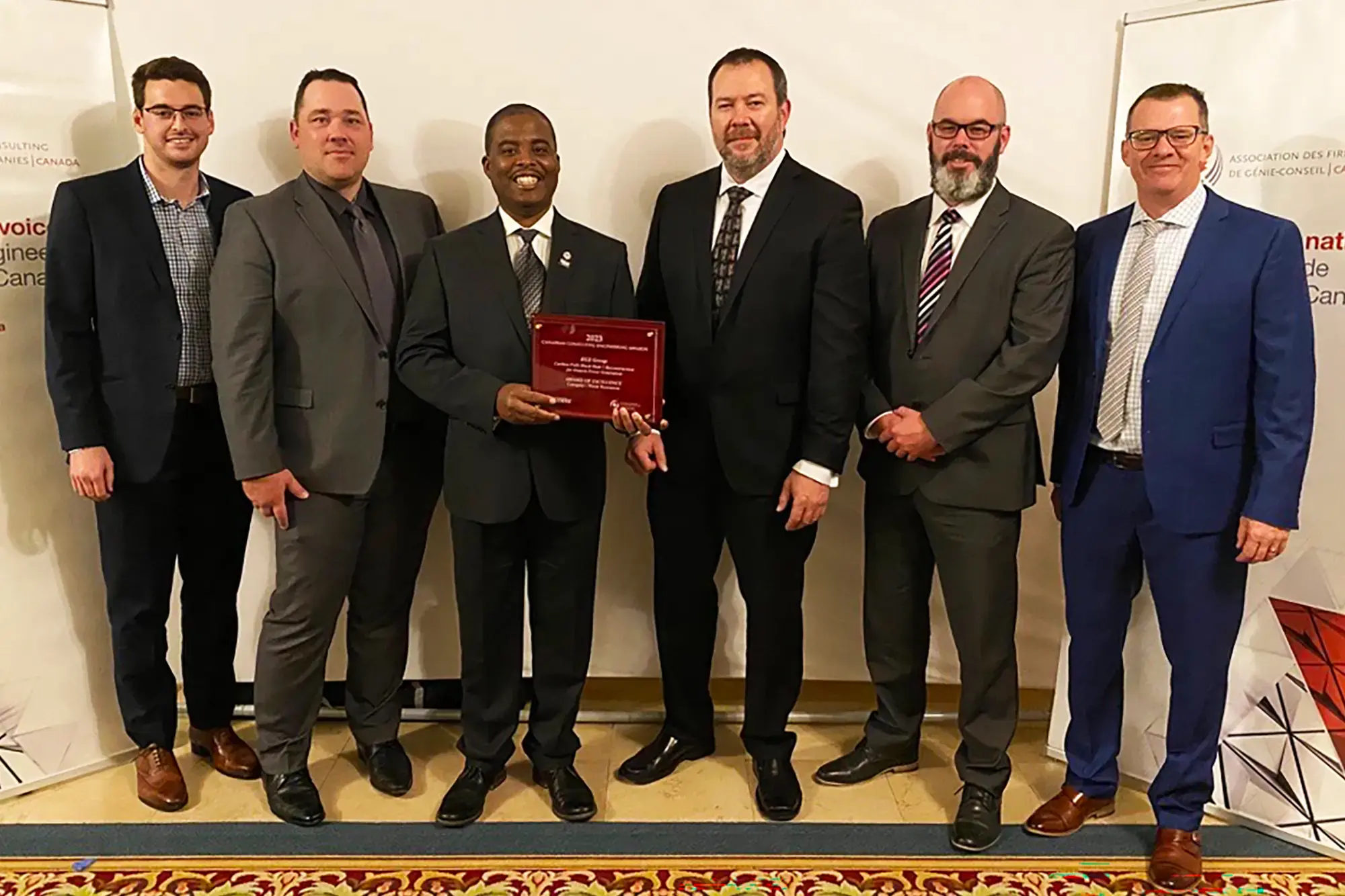 A group of KGS employees dressed in formal business attire proudly accepts their Award of Excellence.