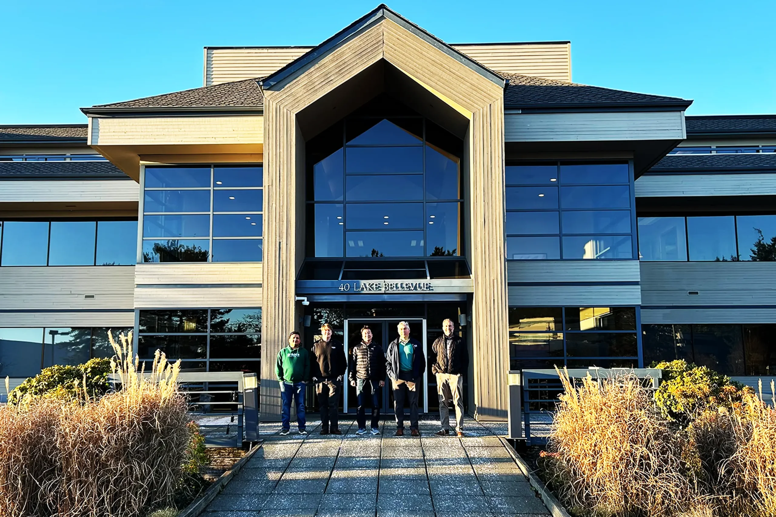 Five casually dressed KGS employees stand in front of a multi-story office building with large glass windows.
