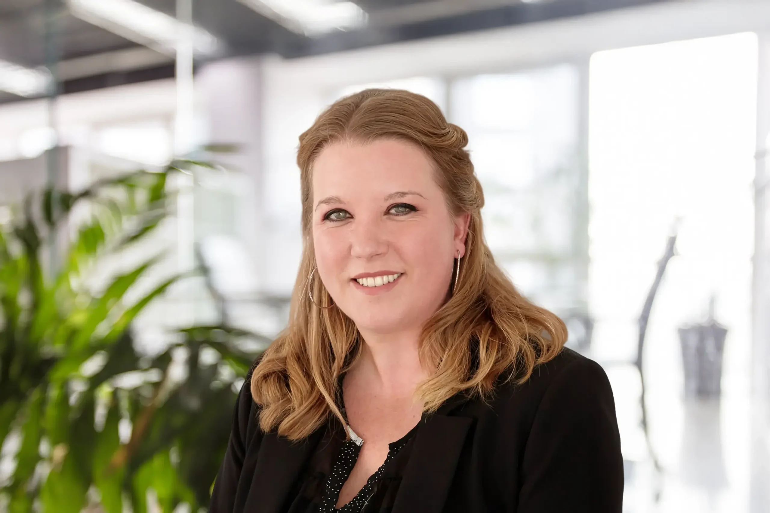 Lindsay Ruel smiles warmly while standing in a plant-filled office setting.