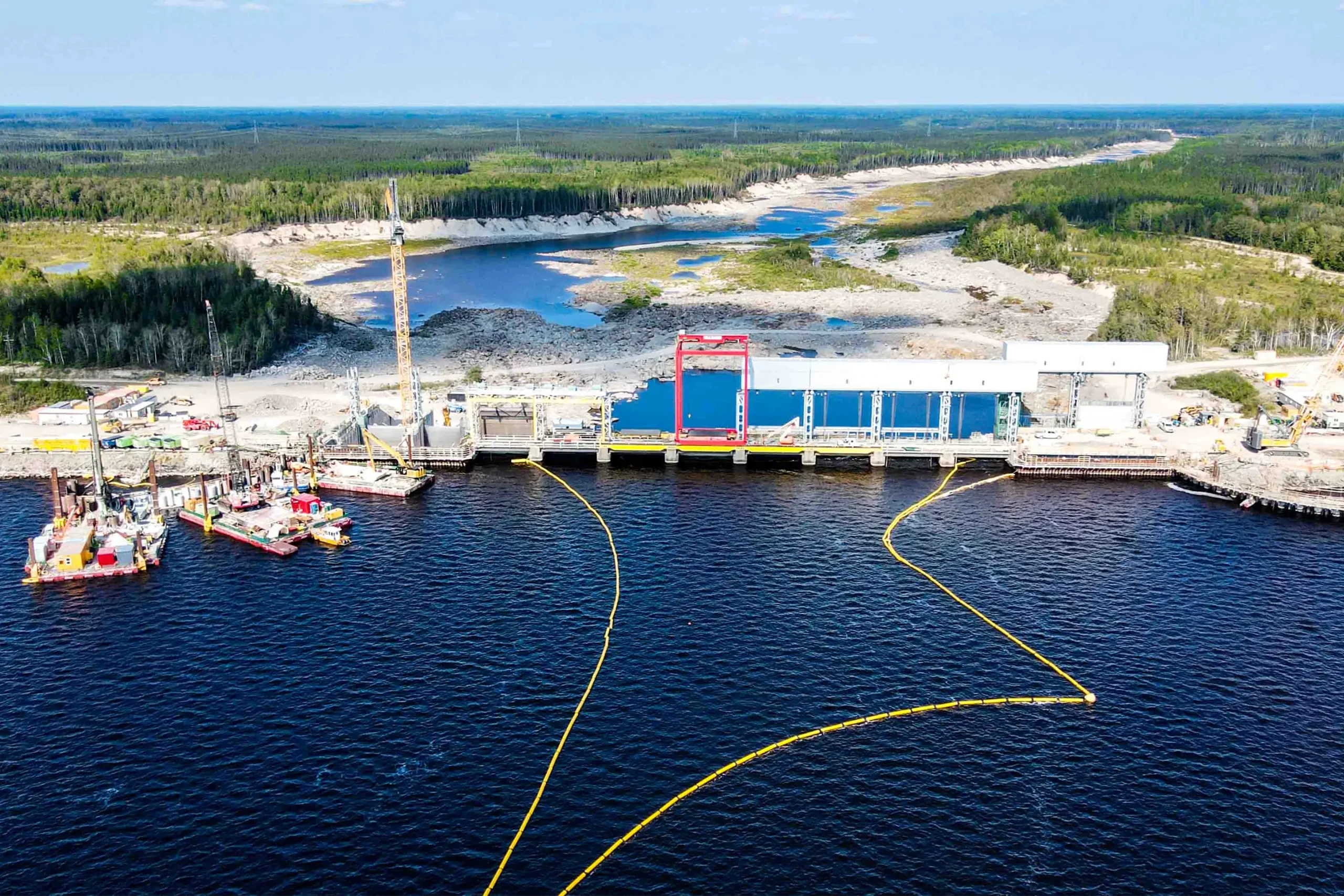 An aerial view of a dam surrounded by a vast body of water and dense forest.