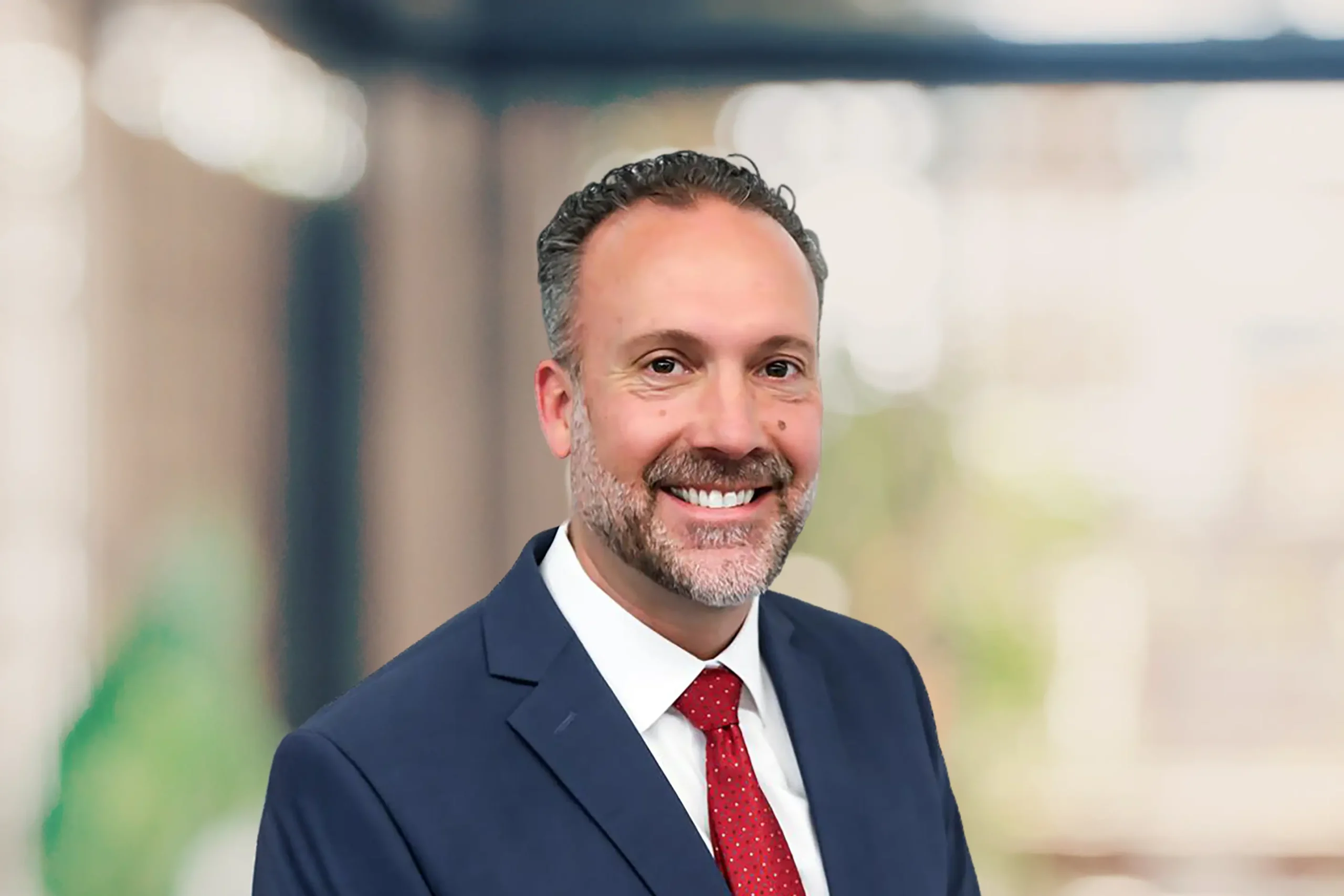 A smiling Nathan Rockwood poses in a navy blue suit and red tie.