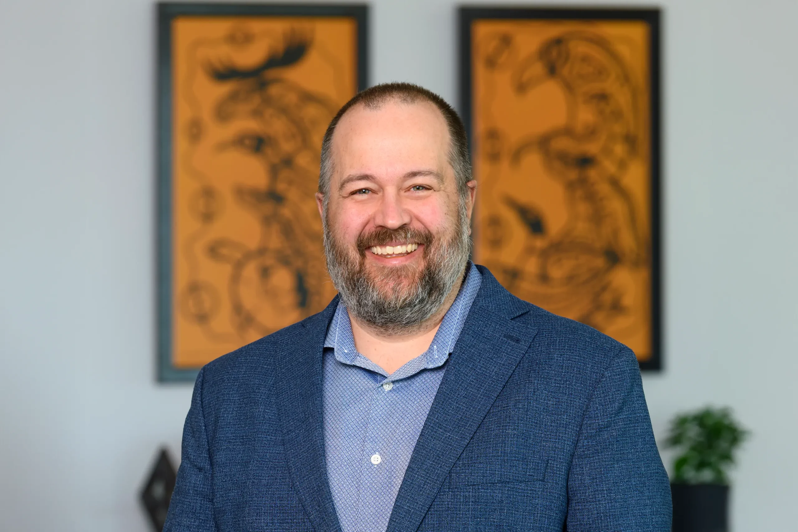 Nathan Ruecker smiles in a navy blazer, standing in front of two paintings.