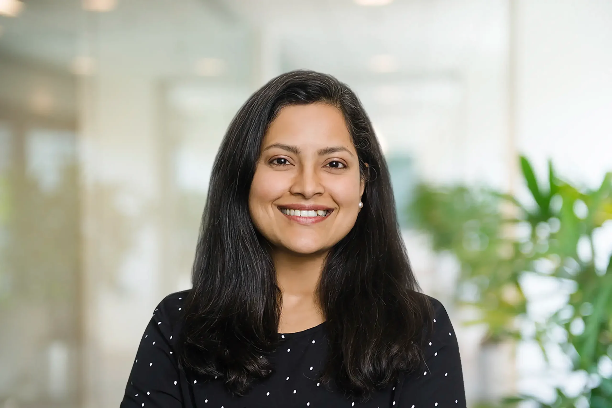 Soni Proctor stands in a plant-filled office, arms confidently crossed and a warm smile on her face.